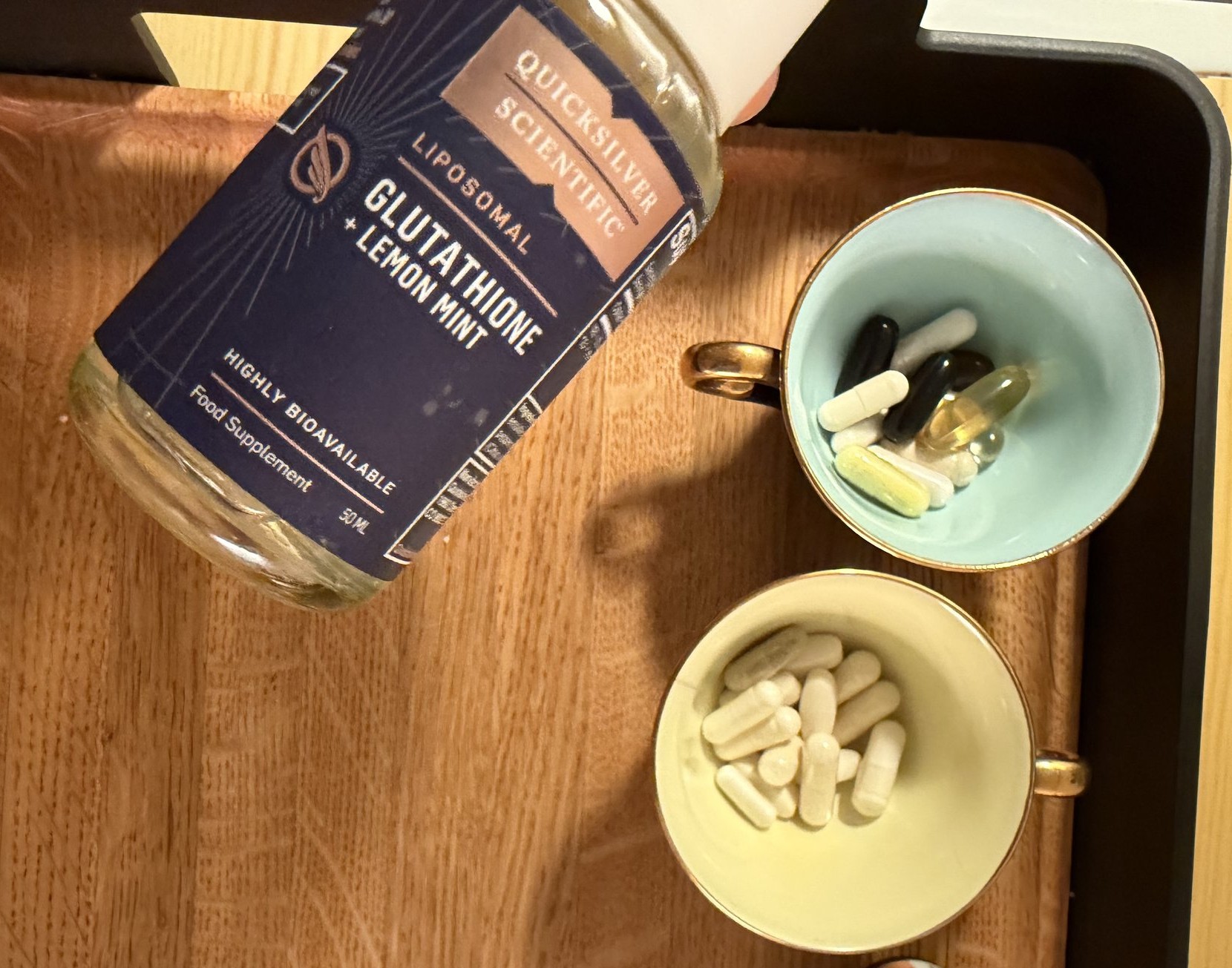 Liposomal glutationflaske på trebrett ved siden av to tekopper med kapsler